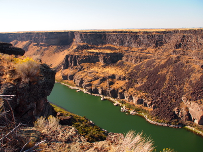 [The full sun gives the water a greenish tint in this area. The canyon walls are shades of yellow and brown beneath the blue sky.]